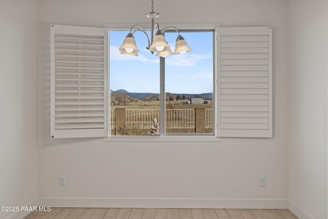 empty room with an inviting chandelier, a mountain view, and light wood-type flooring