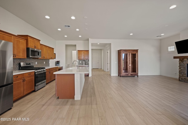 kitchen featuring a kitchen island with sink, backsplash, a stone fireplace, and stainless steel appliances