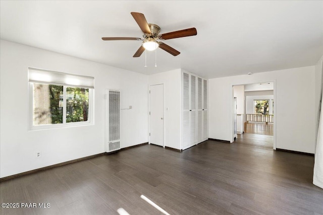 unfurnished room featuring baseboards, a heating unit, dark wood-style flooring, and a ceiling fan