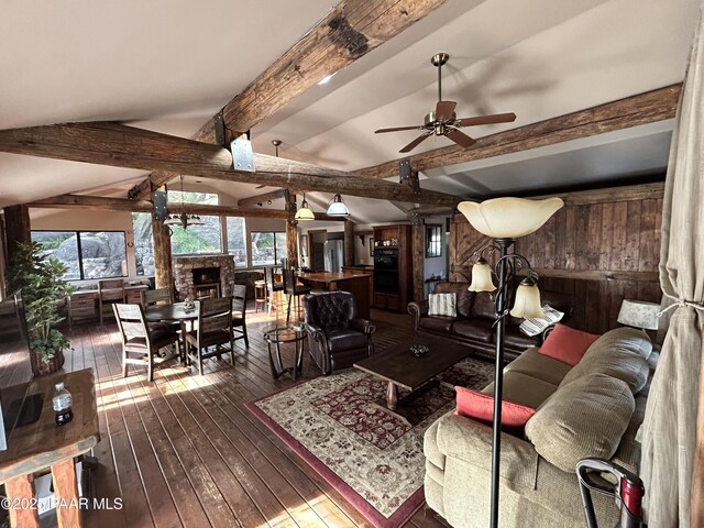 living room featuring lofted ceiling with beams, a stone fireplace, wooden walls, ceiling fan, and dark hardwood / wood-style floors