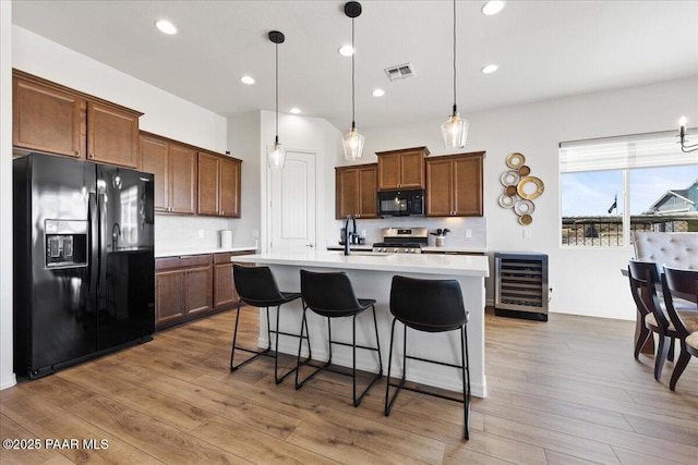 kitchen featuring a kitchen island with sink, wine cooler, black appliances, hanging light fixtures, and sink