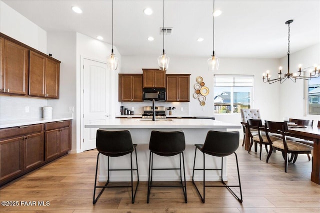 kitchen with a notable chandelier, decorative light fixtures, a kitchen island with sink, and decorative backsplash