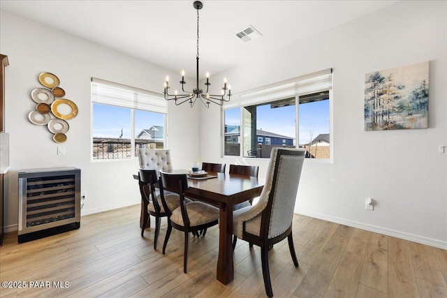 dining space featuring a notable chandelier, beverage cooler, and light wood-type flooring