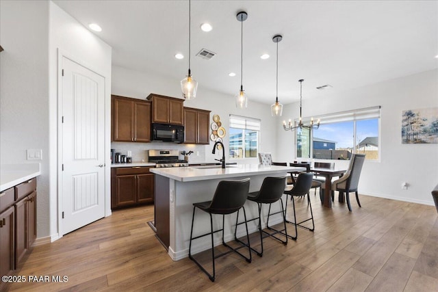 kitchen featuring sink, decorative light fixtures, stainless steel range oven, an island with sink, and a breakfast bar