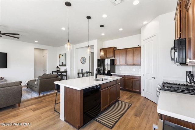 kitchen featuring a kitchen island with sink, black appliances, pendant lighting, hardwood / wood-style flooring, and sink