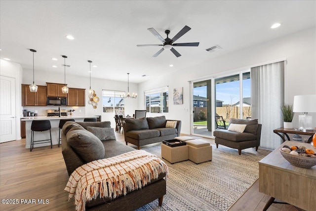 living room with light wood-type flooring and ceiling fan with notable chandelier