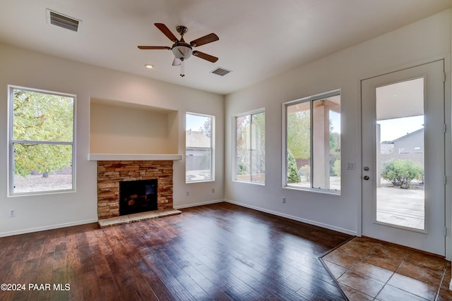 unfurnished living room featuring ceiling fan, dark hardwood / wood-style flooring, and a stone fireplace