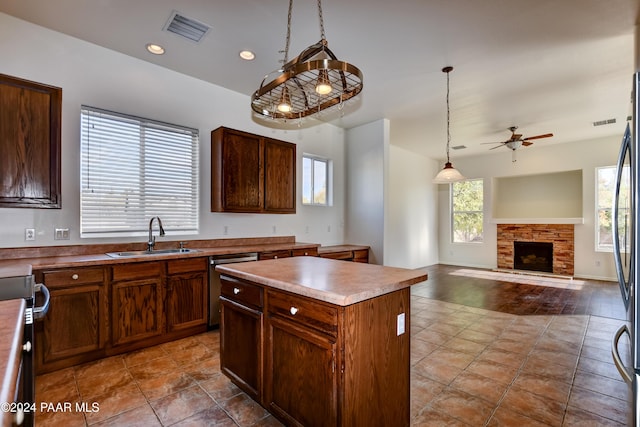 kitchen with sink, stainless steel dishwasher, pendant lighting, a fireplace, and a kitchen island