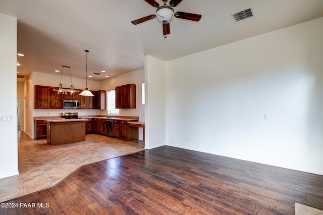 kitchen featuring pendant lighting, ceiling fan, light wood-type flooring, a kitchen island, and stainless steel appliances