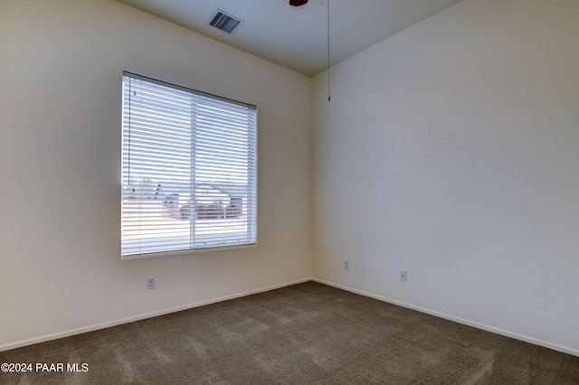 empty room featuring dark colored carpet, ceiling fan, and a wealth of natural light