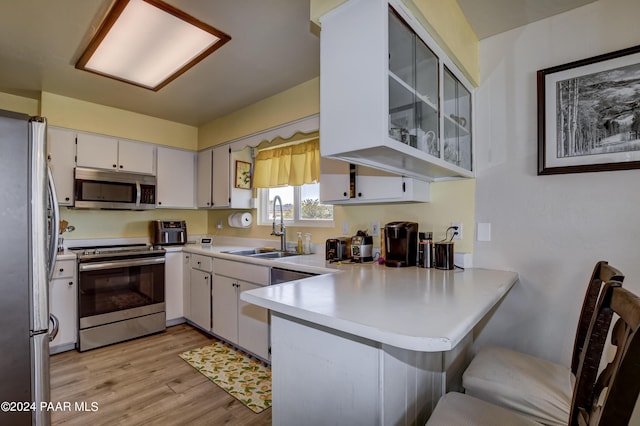 kitchen featuring kitchen peninsula, appliances with stainless steel finishes, sink, light hardwood / wood-style flooring, and white cabinets