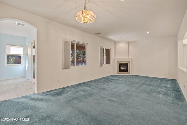 unfurnished living room featuring carpet, an inviting chandelier, and a tile fireplace