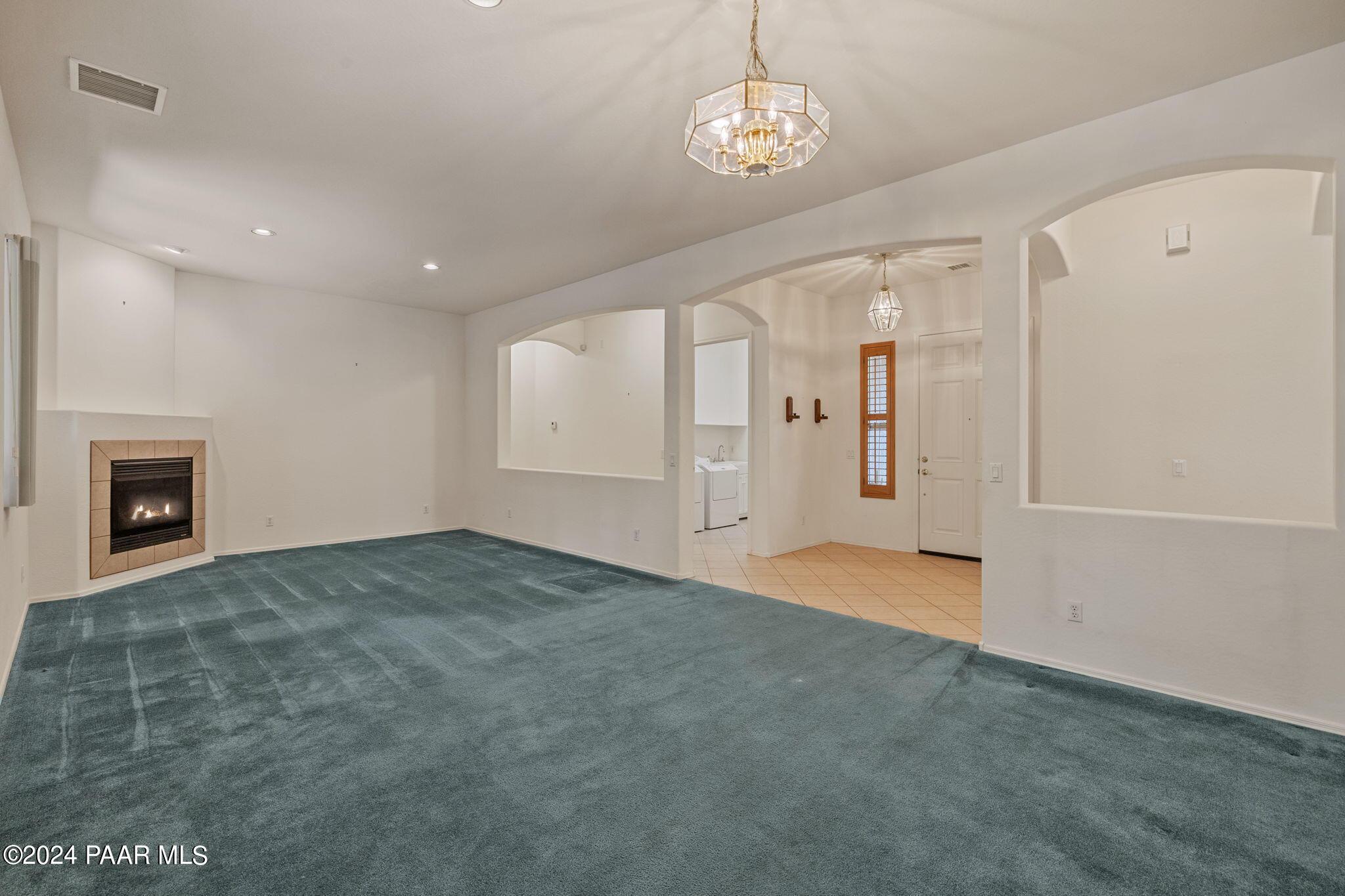 unfurnished living room with a fireplace, light colored carpet, an inviting chandelier, and separate washer and dryer