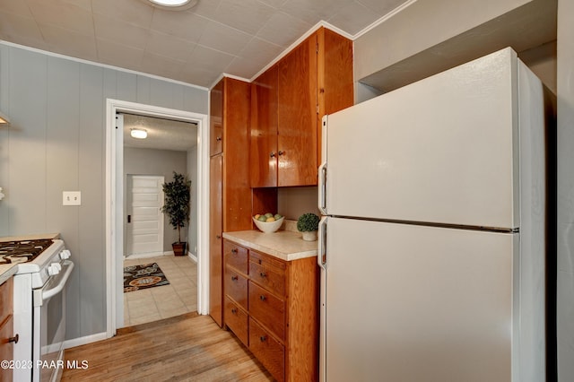 kitchen with crown molding, white appliances, light hardwood / wood-style floors, and wood walls