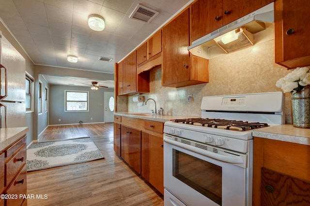 kitchen featuring tasteful backsplash, white gas range, sink, ceiling fan, and light hardwood / wood-style flooring