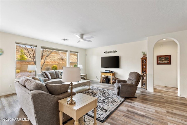 living room with plenty of natural light, light wood-type flooring, arched walkways, and ceiling fan