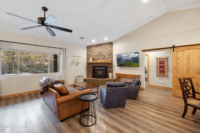 living room with vaulted ceiling, a stone fireplace, hardwood / wood-style floors, ceiling fan, and a barn door