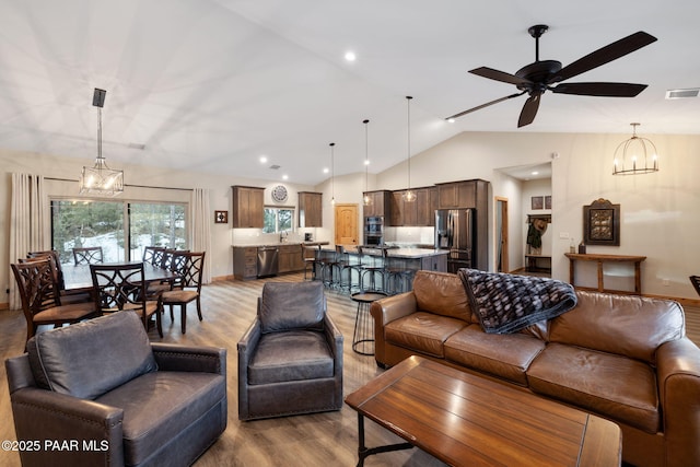 living room featuring vaulted ceiling, ceiling fan with notable chandelier, sink, and hardwood / wood-style floors