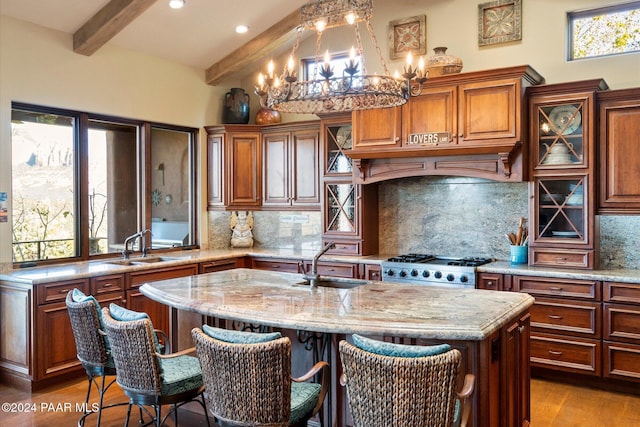 kitchen with beam ceiling, decorative backsplash, a kitchen island with sink, and sink