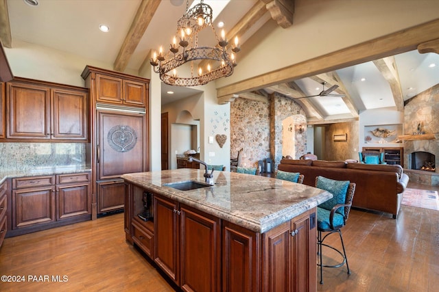 kitchen featuring a fireplace, sink, lofted ceiling with beams, and a center island with sink