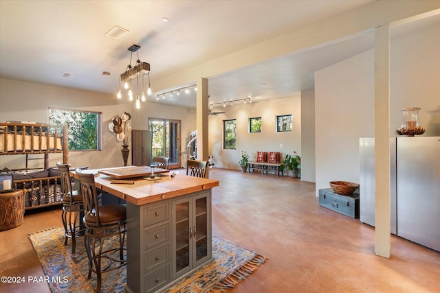 kitchen featuring wood counters, stainless steel fridge, ceiling fan, pendant lighting, and a breakfast bar area