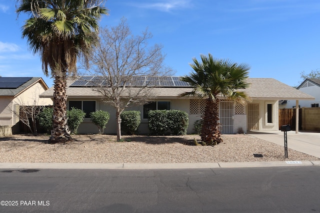 ranch-style house with solar panels, a shingled roof, fence, driveway, and stucco siding