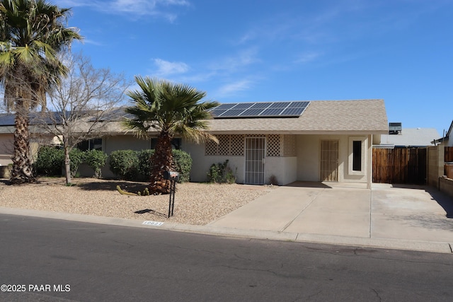 single story home featuring roof mounted solar panels, roof with shingles, fence, and stucco siding