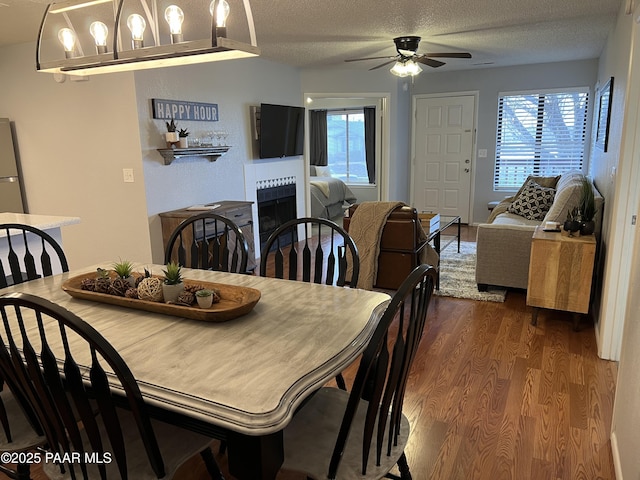 dining area with dark wood-style floors, a ceiling fan, plenty of natural light, a tiled fireplace, and a textured ceiling