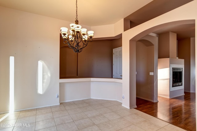 unfurnished dining area featuring a multi sided fireplace, light tile patterned floors, and a chandelier