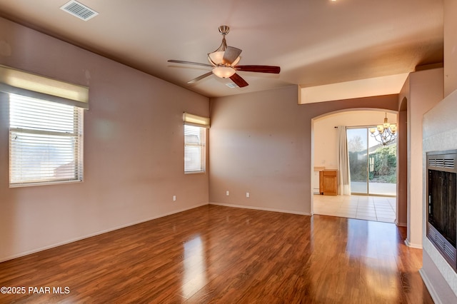 unfurnished living room with ceiling fan with notable chandelier, hardwood / wood-style floors, and a tiled fireplace