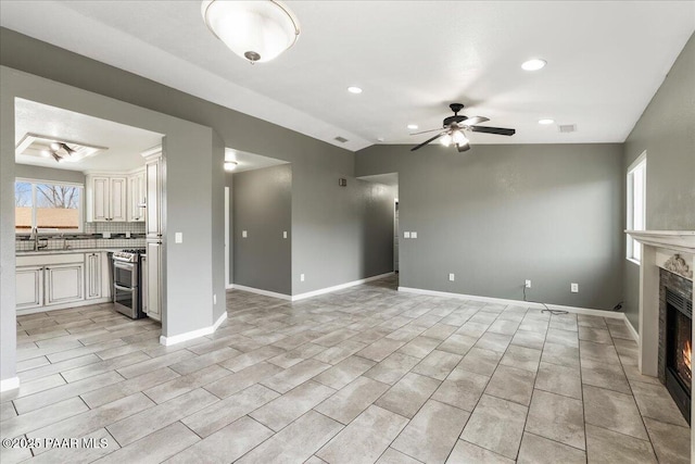 unfurnished living room with ceiling fan, baseboards, lofted ceiling, a lit fireplace, and a sink