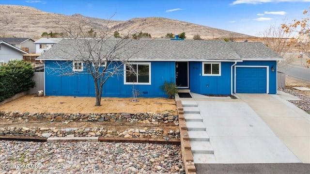 ranch-style house featuring fence, roof with shingles, an attached garage, concrete driveway, and a mountain view