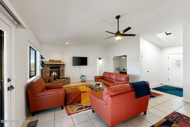 living room featuring ceiling fan, a fireplace, vaulted ceiling with skylight, and light tile patterned floors