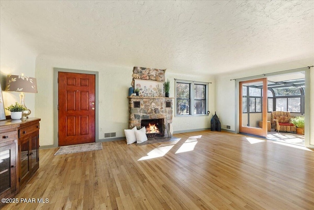 unfurnished living room featuring a stone fireplace, a textured ceiling, and light wood-type flooring