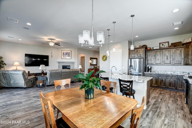 dining room with ceiling fan with notable chandelier, wood-type flooring, and sink