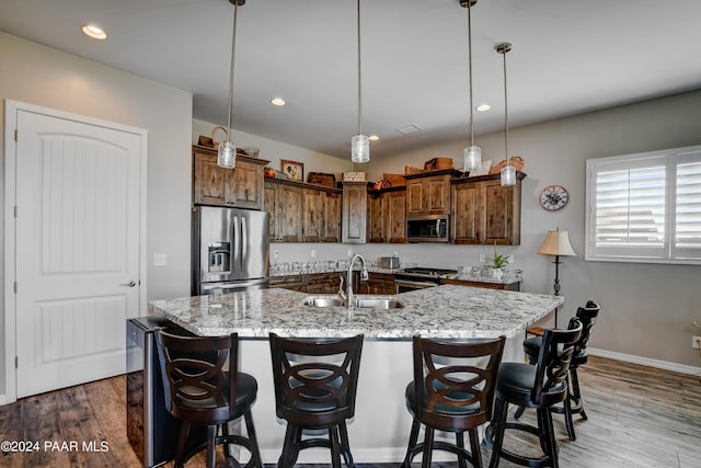 kitchen featuring stainless steel appliances, sink, wood-type flooring, a large island with sink, and decorative light fixtures