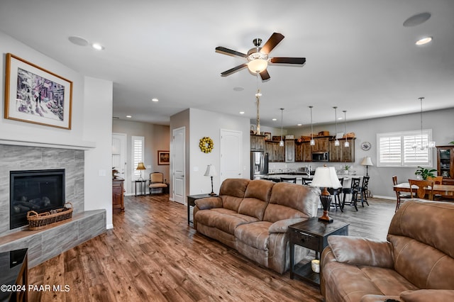 living room featuring a fireplace, wood-type flooring, and ceiling fan with notable chandelier