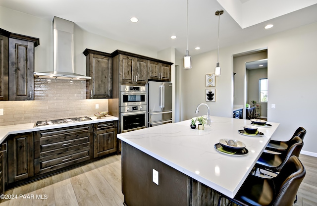 kitchen featuring appliances with stainless steel finishes, light wood-type flooring, dark brown cabinets, and wall chimney exhaust hood