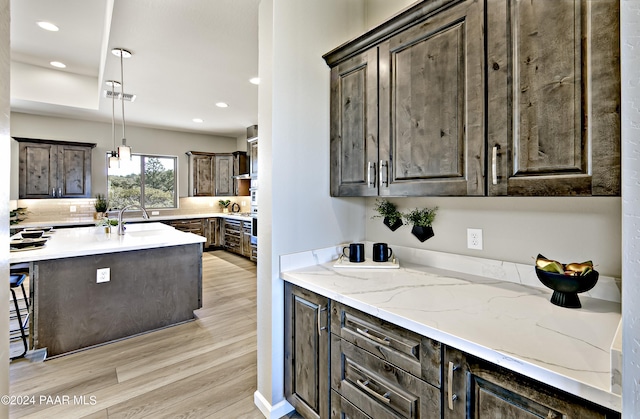 kitchen featuring recessed lighting, light wood-style floors, visible vents, light stone counters, and dark brown cabinets