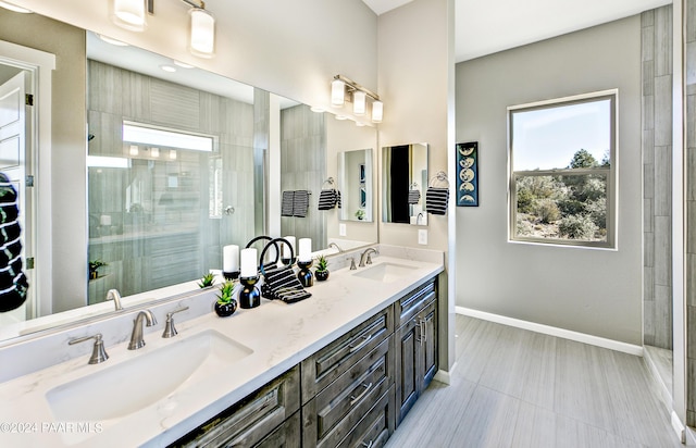 bathroom with double vanity, baseboards, tiled shower, and a sink