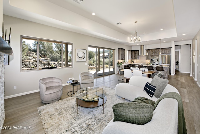 living area with a raised ceiling, baseboards, recessed lighting, dark wood-type flooring, and a notable chandelier