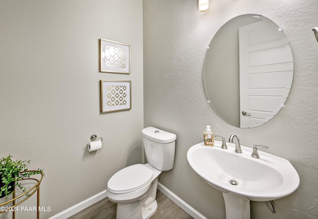 bathroom featuring baseboards, wood finished floors, toilet, and a sink