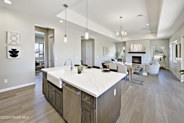kitchen featuring a sink, light wood-style floors, a stone fireplace, dishwasher, and dark brown cabinets