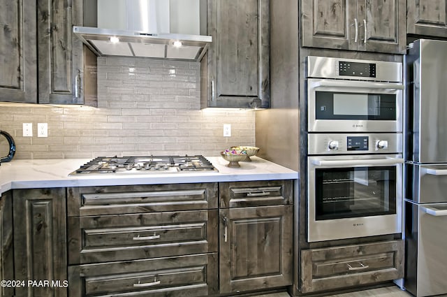 kitchen featuring decorative backsplash, stainless steel appliances, dark brown cabinets, light stone countertops, and ventilation hood