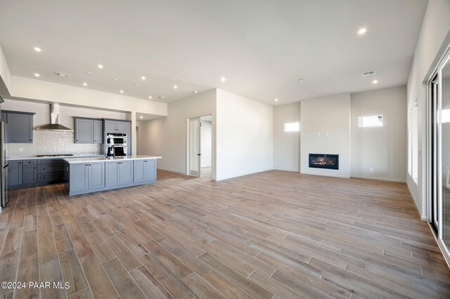 kitchen featuring light wood-type flooring, an island with sink, wall chimney exhaust hood, and appliances with stainless steel finishes