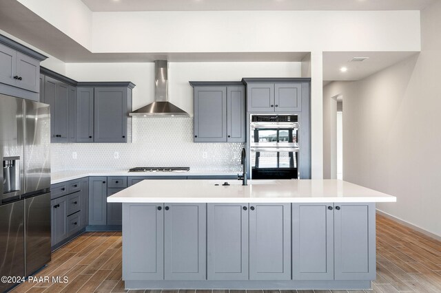 kitchen with a kitchen island with sink, gray cabinetry, wall chimney exhaust hood, and appliances with stainless steel finishes