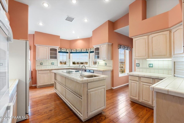 kitchen featuring glass insert cabinets, visible vents, a center island with sink, and light wood-type flooring