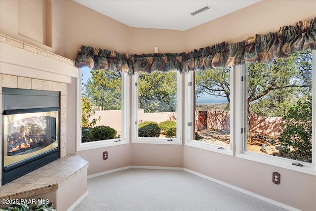 unfurnished room with visible vents, carpet floors, baseboards, and a tiled fireplace