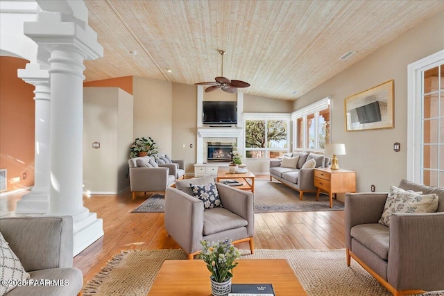 living room with a glass covered fireplace, decorative columns, wooden ceiling, and light wood-style flooring