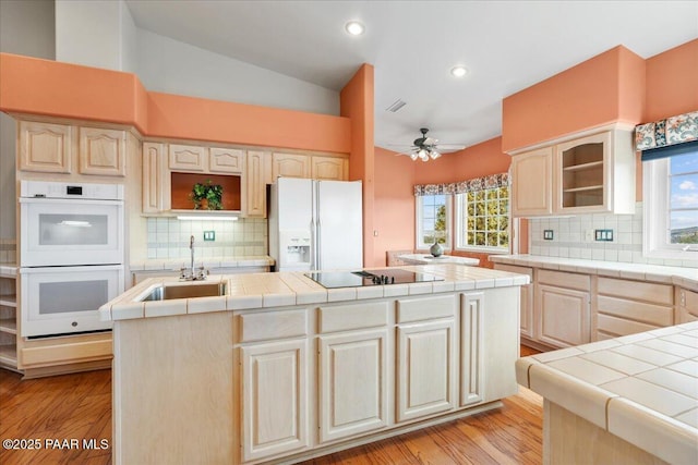 kitchen with white appliances, tile countertops, lofted ceiling, a sink, and a center island